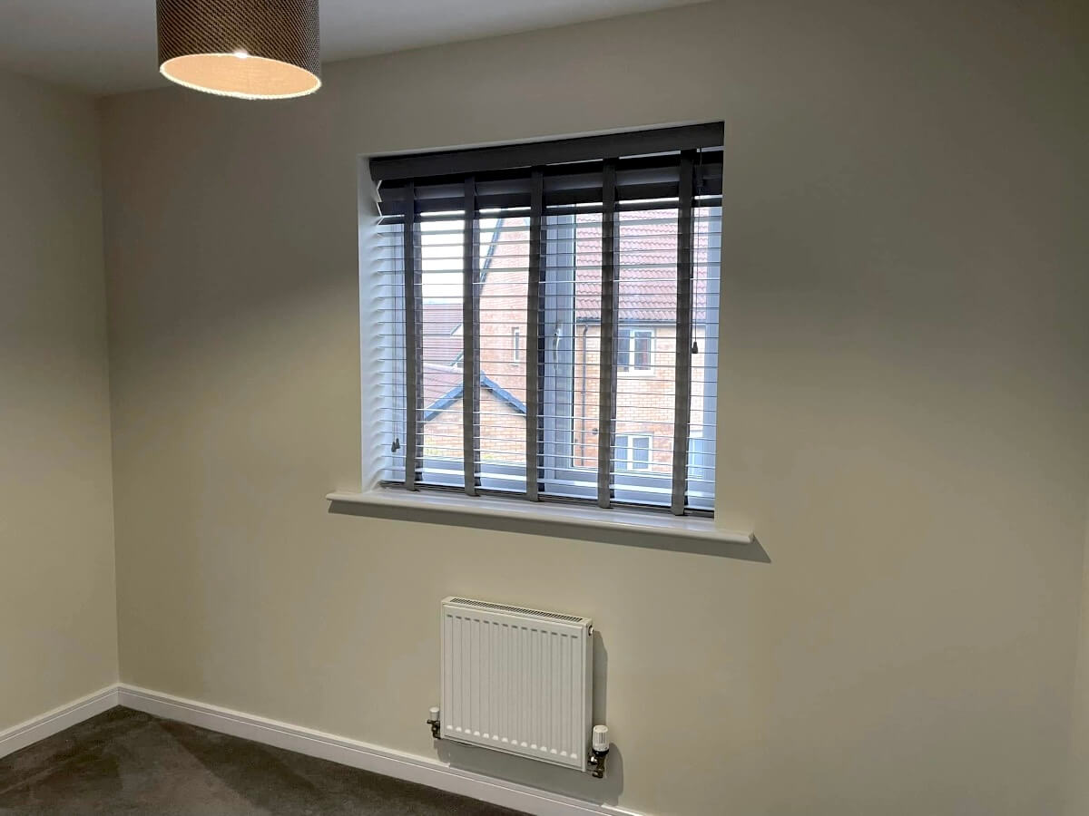 Bedroom with clean beige painted walls, a white radiator and a window with blinds